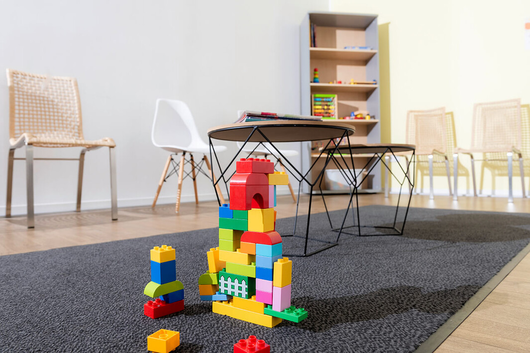 Raum mit buntem Spielzeug auf Teppich, Stühle im Hintergrund – für kindgerechte Sprechstunde.